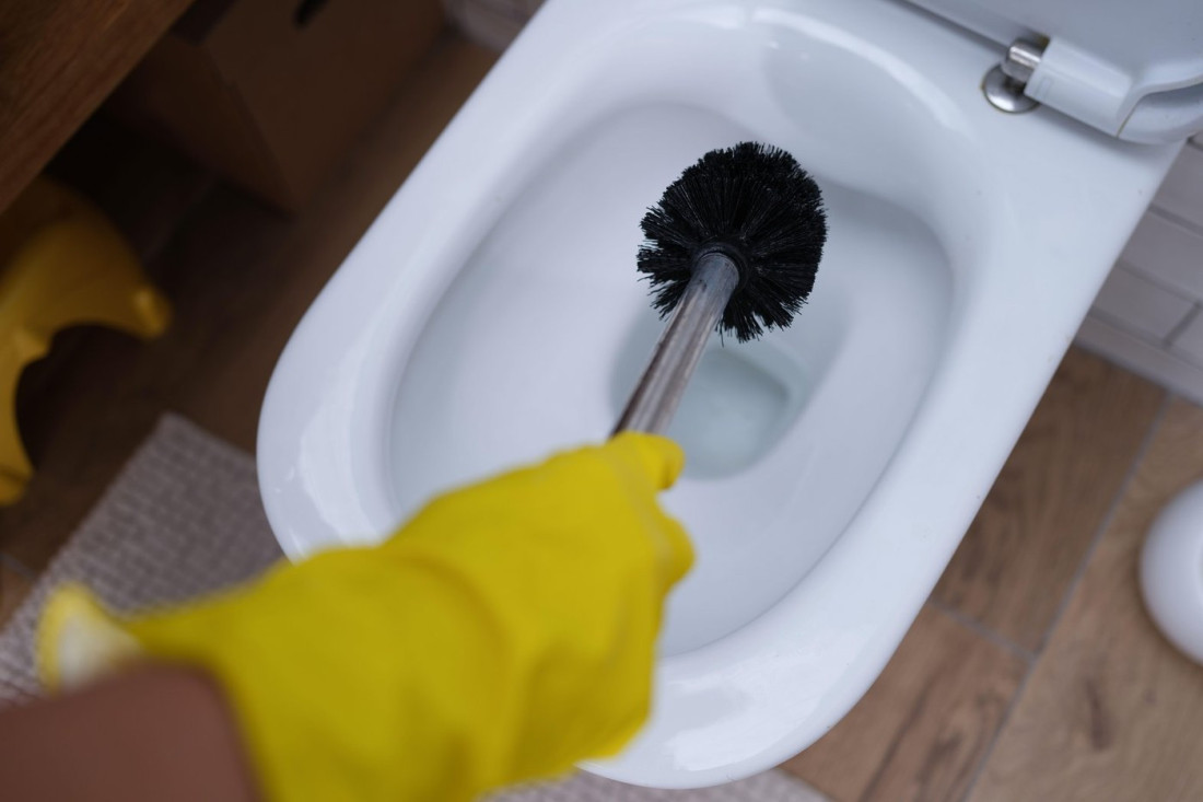 手袋をした手がトイレブラシで便器を掃除している